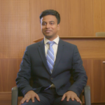 university student wearing a suit and tie sitting in a chair with his hands in his lap