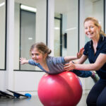 Adelaide University occupational therapy student working with child on a red ball