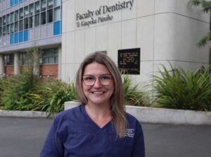Learn more about Otago's Bachelor of Dental Surgery degree young woman with glasses standing outside a building that says Faculty of Dentistry