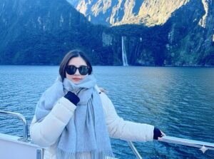woman wearing winter clote=hes standing in front of water and mountains